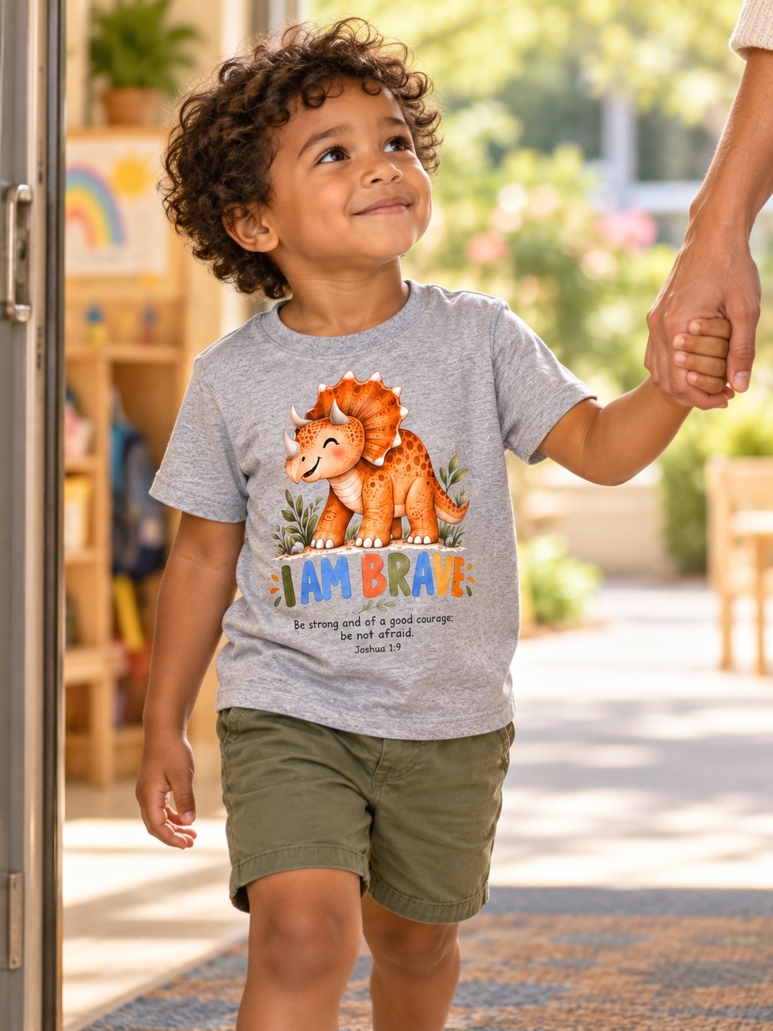 Child wearing an I Am Brave dinosaur shirt holding an adult's hand on the way to school.