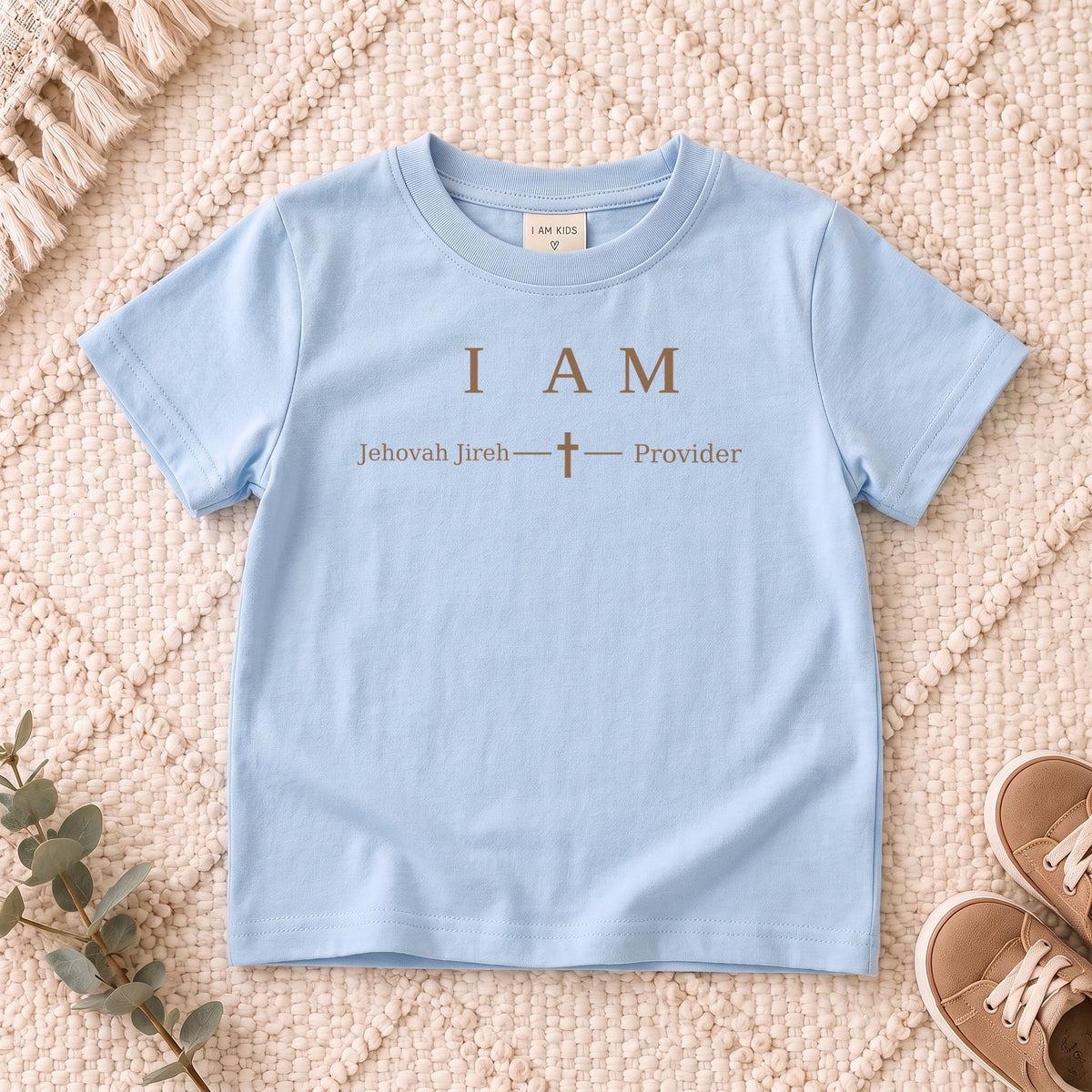 I AM Kids Jehovah Jireh — Provider | The Great I AM Collection design on a Light Blue shirt, shown on a cream rug.