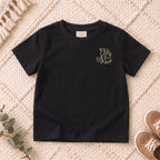 I AM Kids Crowned JC Jesus Christ Kids Tee | Left Chest design on a Black shirt, shown on a cream rug.