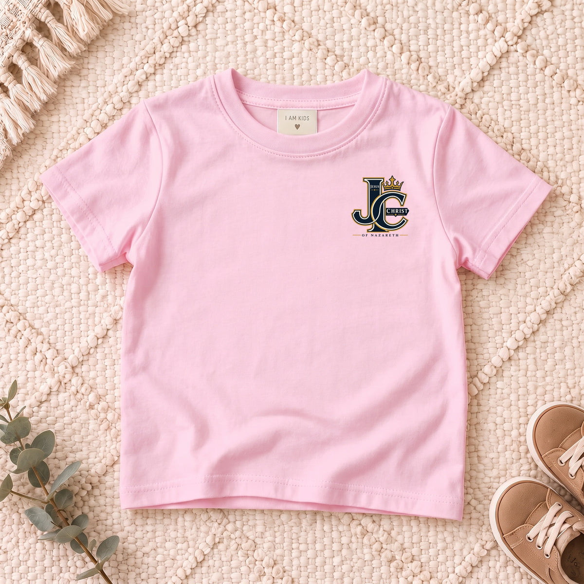 I AM Kids Crowned JC Jesus Christ Kids Tee | Left Chest design on a Light Pink shirt, shown on a cream rug.