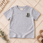 I AM Kids Crowned JC Jesus Christ Kids Tee | Left Chest design on a Sport Grey shirt, shown on a cream rug.