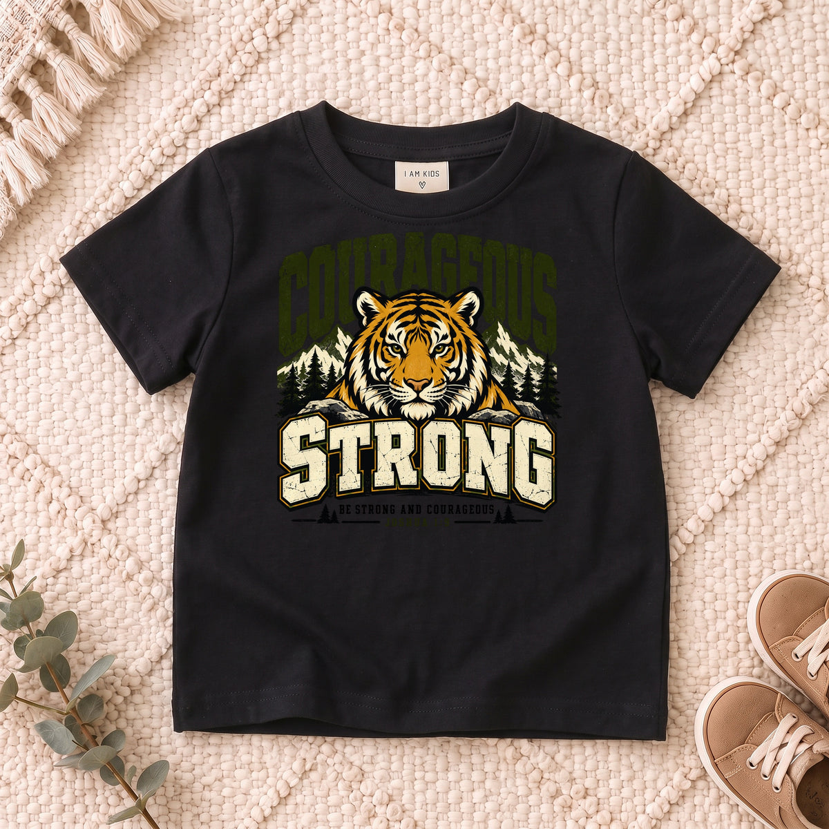 I AM Kids Be Strong & Courageous Tiger Kids Tee design on a Black shirt, shown on a cream rug.