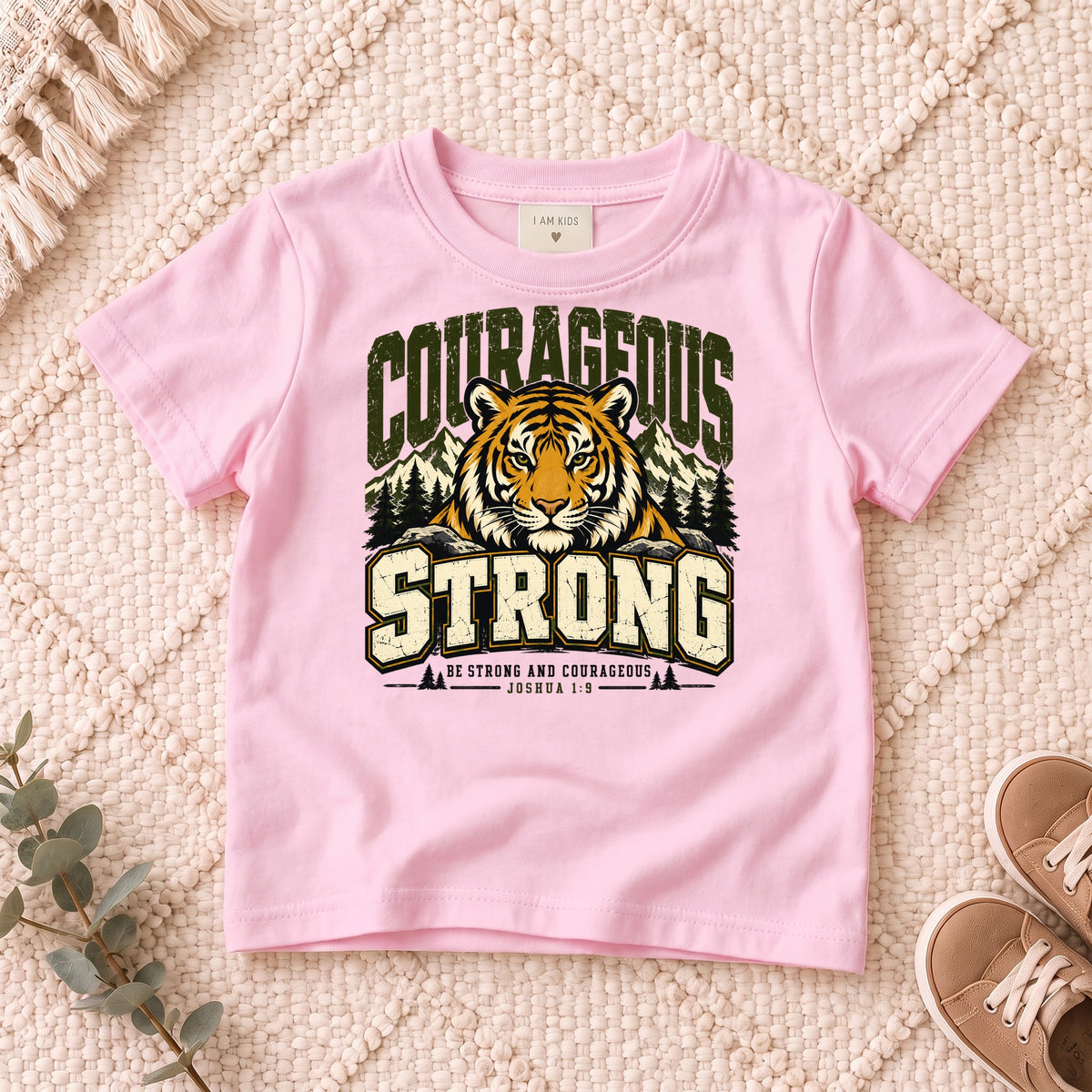 I AM Kids Be Strong & Courageous Tiger Kids Tee design on a Light Pink shirt, shown on a cream rug.