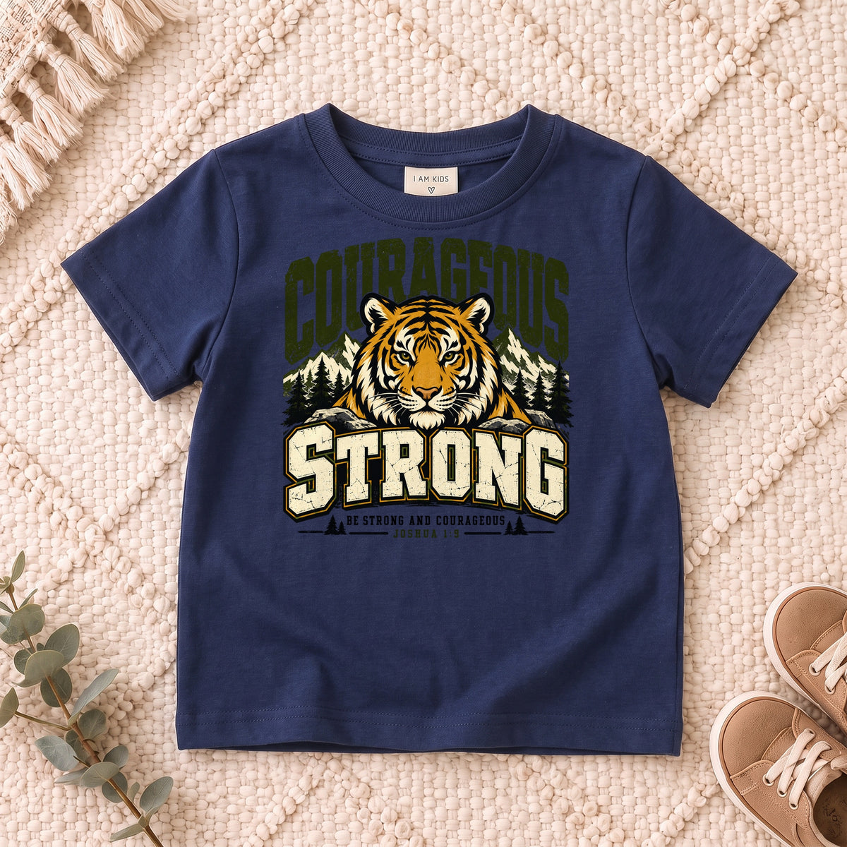 I AM Kids Be Strong & Courageous Tiger Kids Tee design on a Navy shirt, shown on a cream rug.