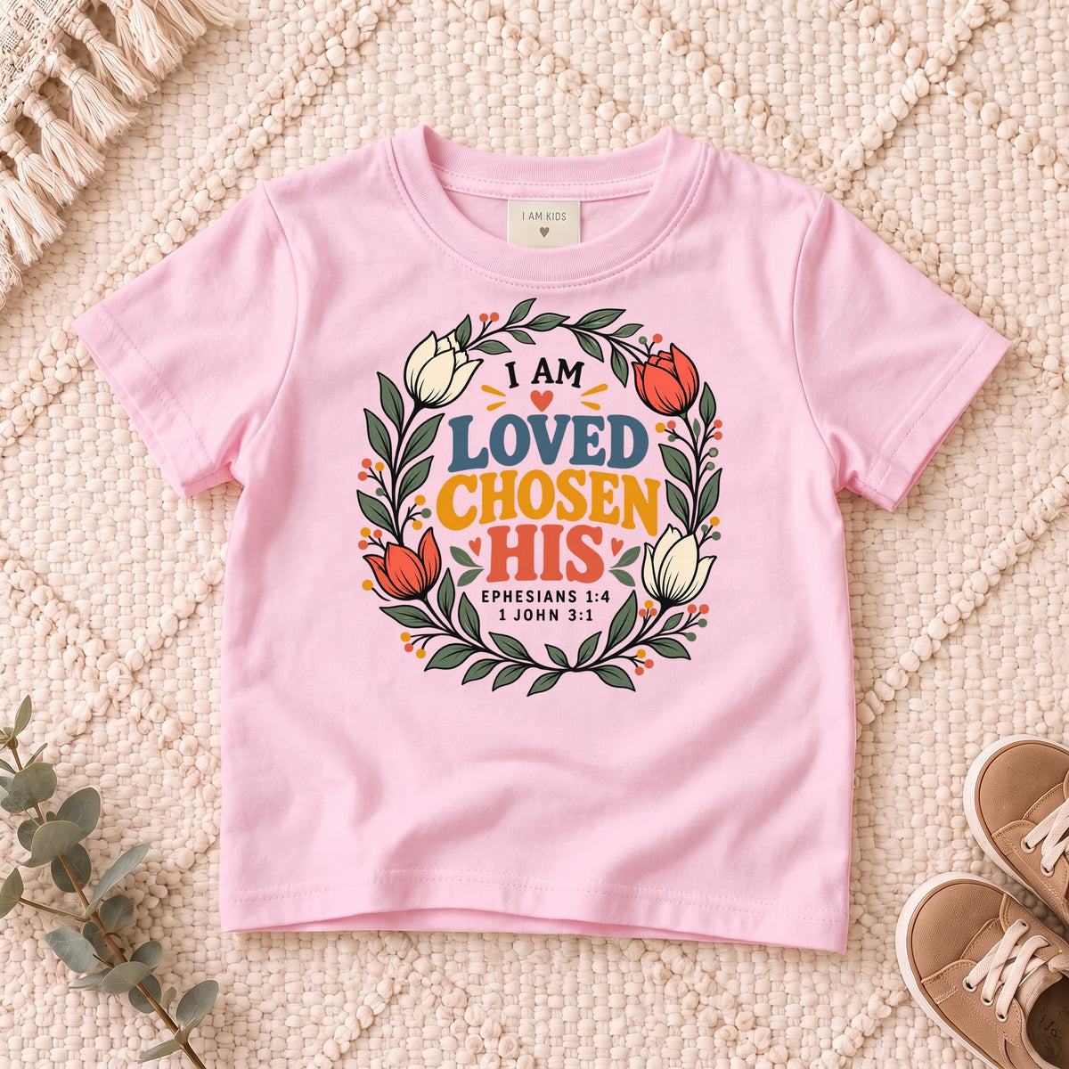 I AM Kids I AM Loved, Chosen & His Floral Wreath Kids Tee design on a Light Pink shirt, shown on a cream rug.