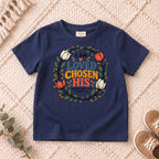 I AM Kids I AM Loved, Chosen & His Floral Wreath Kids Tee design on a Navy shirt, shown on a cream rug.