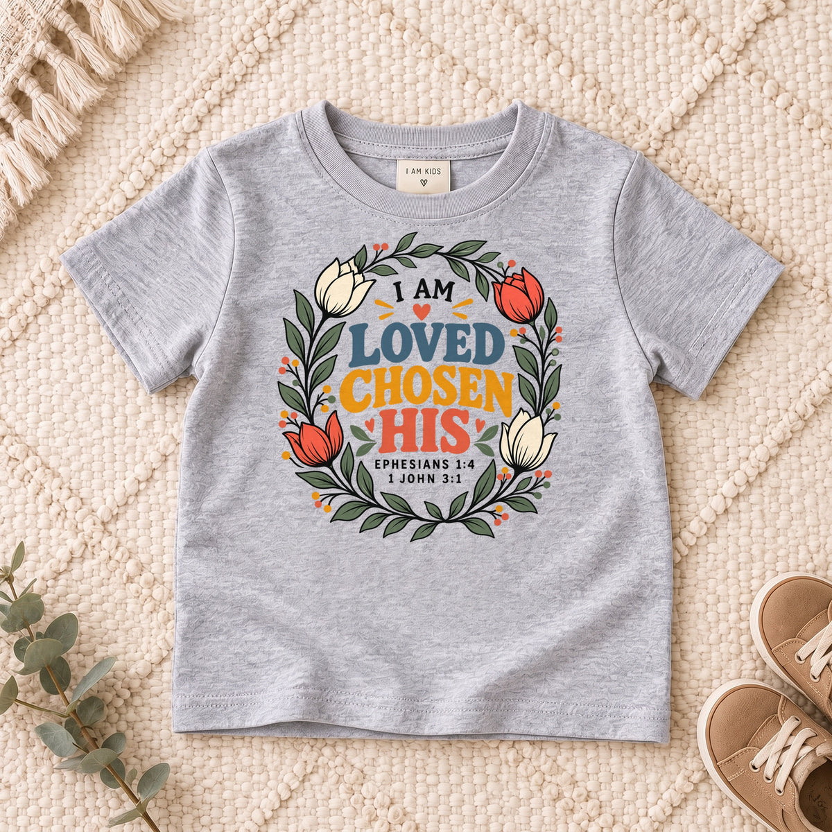 I AM Kids I AM Loved, Chosen & His Floral Wreath Kids Tee design on a Sport Grey shirt, shown on a cream rug.