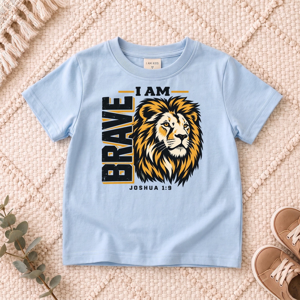 I AM Kids I AM Brave Lion Kids Tee | Joshua 1:9 design on a Light Blue shirt, shown on a cream rug.
