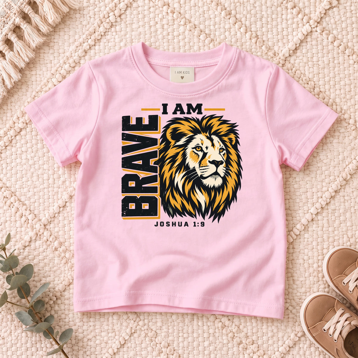 I AM Kids I AM Brave Lion Kids Tee | Joshua 1:9 design on a Light Pink shirt, shown on a cream rug.