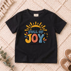 I AM Kids I AM Full of Joy Sunshine Kids Tee | Romans 15:13 design on a Black shirt, shown on a cream rug.