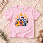 I AM Kids I AM Full of Joy Sunshine Kids Tee | Romans 15:13 design on a Light Pink shirt, shown on a cream rug.