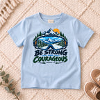 I AM Kids Be Strong & Courageous Mountain Goggles Kids Tee | Joshua 1:9 design on a Light Blue shirt, shown on a cream rug.
