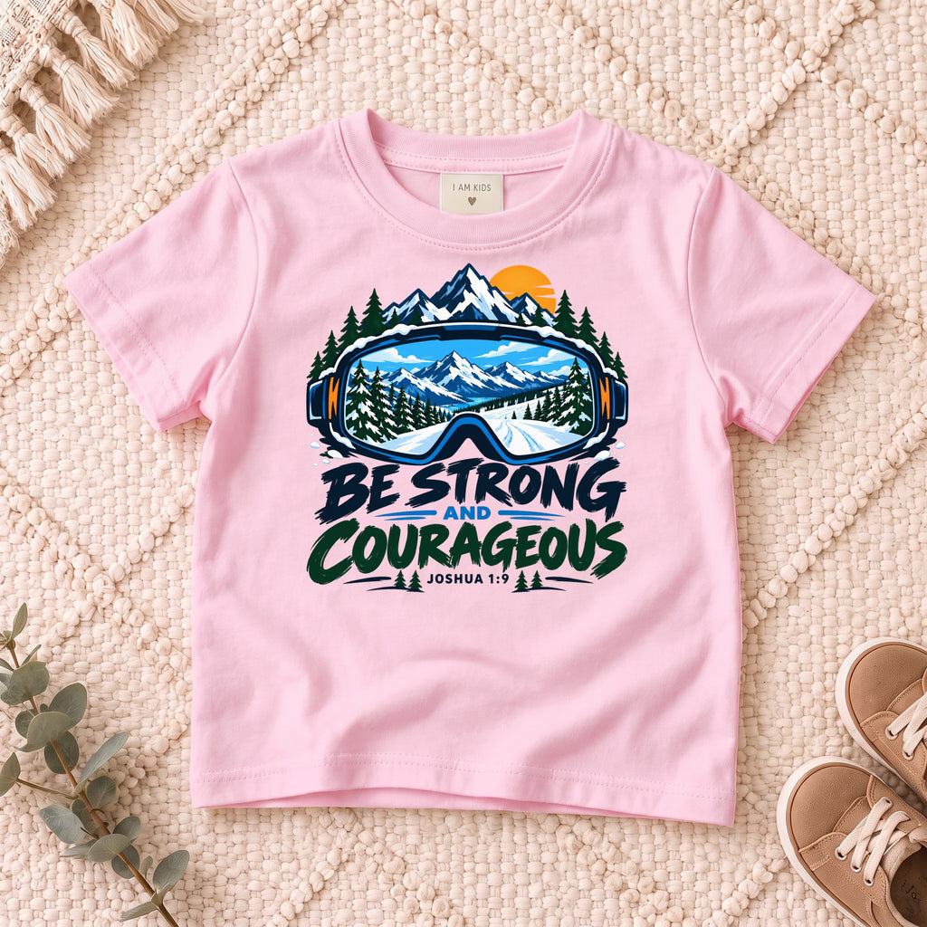 I AM Kids Be Strong & Courageous Mountain Goggles Kids Tee | Joshua 1:9 design on a Light Pink shirt, shown on a cream rug.