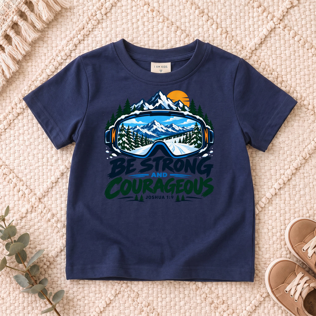 I AM Kids Be Strong & Courageous Mountain Goggles Kids Tee | Joshua 1:9 design on a Navy shirt, shown on a cream rug.