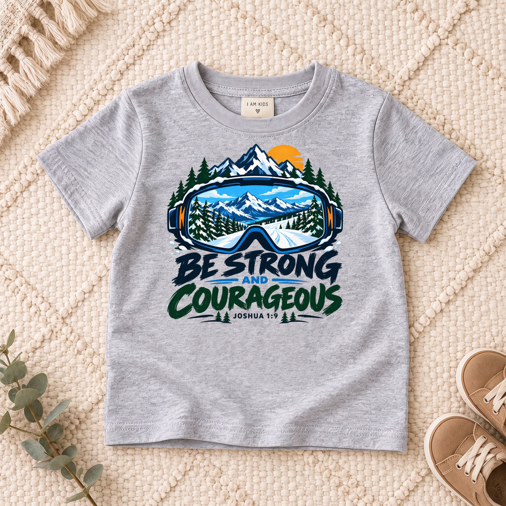 I AM Kids Be Strong & Courageous Mountain Goggles Kids Tee | Joshua 1:9 design on a Sport Grey shirt, shown on a cream rug.