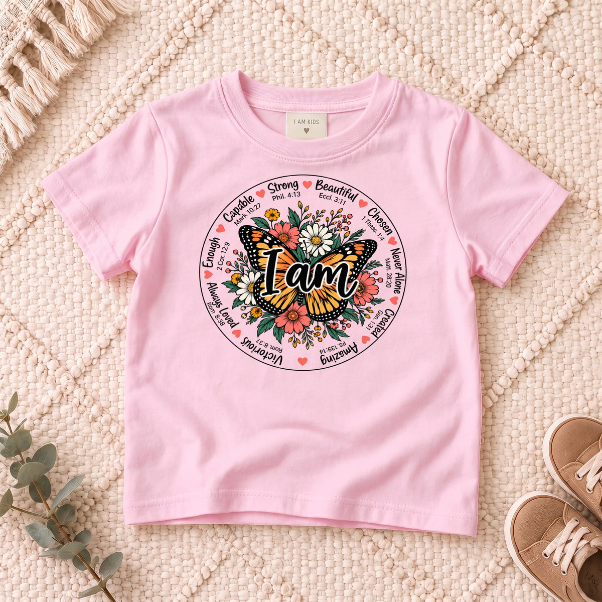 I AM Kids I AM Butterfly Words of Faith Kids Tee design on a Light Pink shirt, shown on a cream rug.