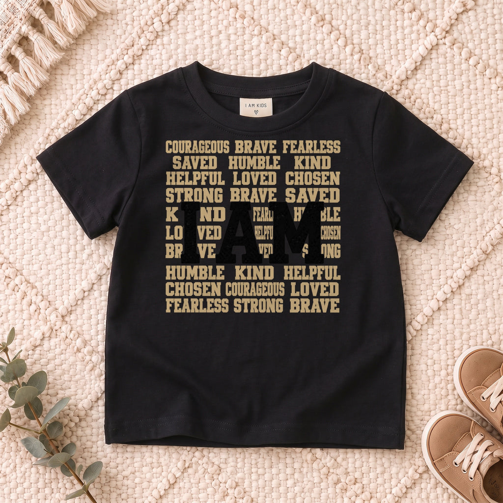 I AM Kids I AM Words of Faith Kids Tee design on a Black shirt, shown on a cream rug.