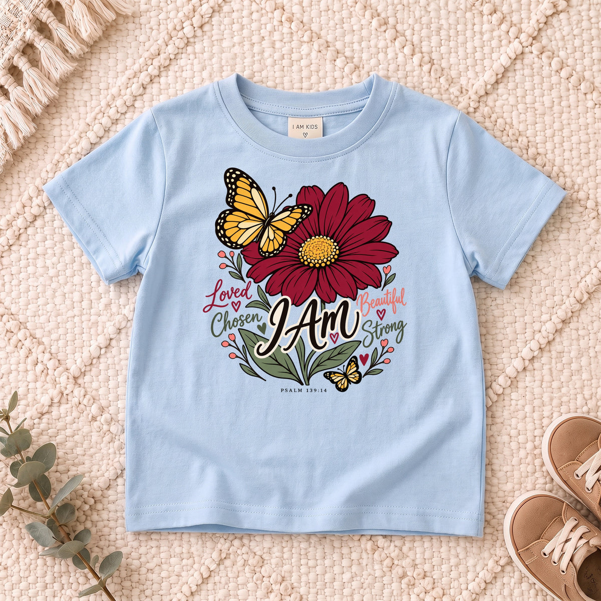 I AM Kids I AM Loved & Chosen Burgundy Flower Kids Tee | Psalm 139:14 design on a Light Blue shirt, shown on a cream rug.