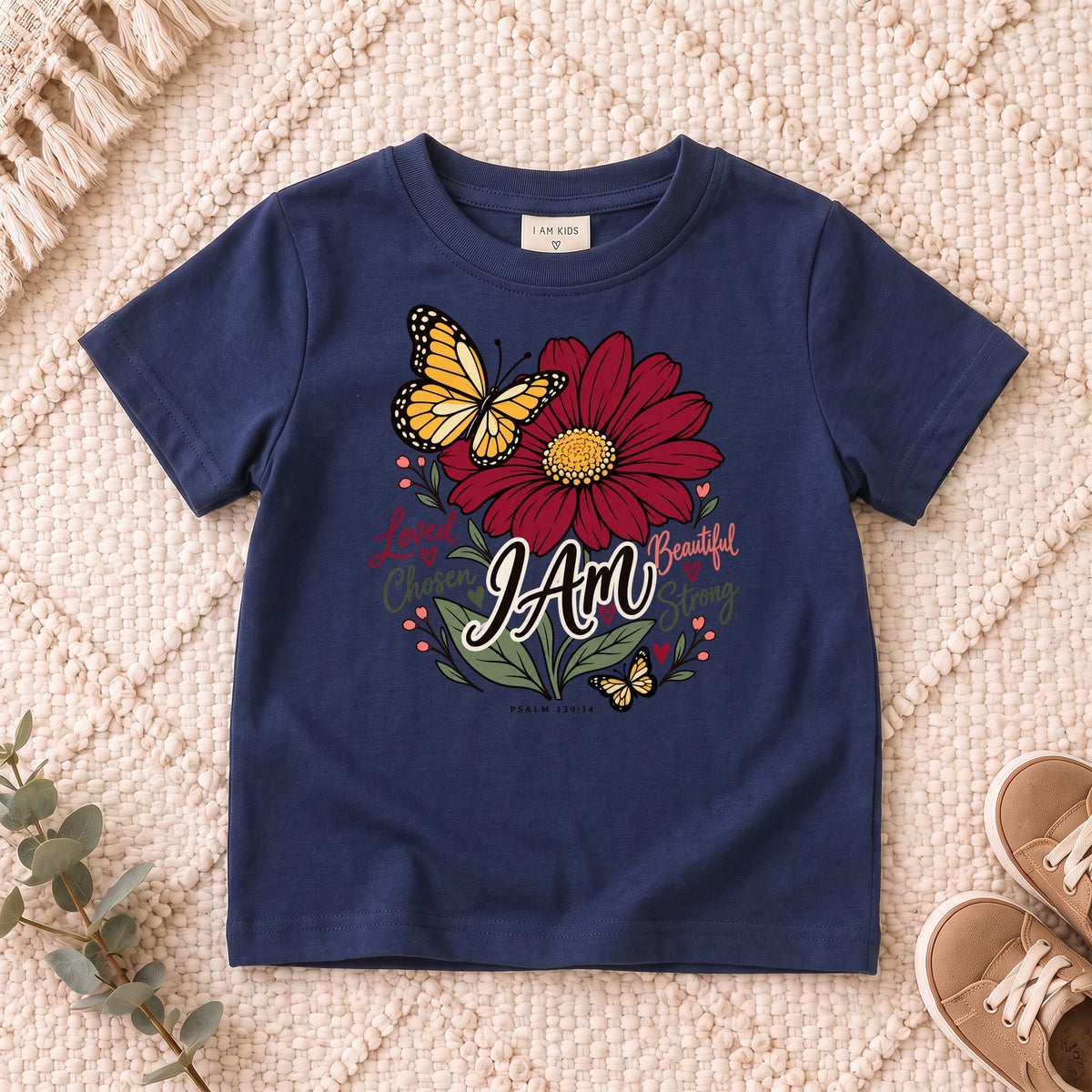 I AM Kids I AM Loved & Chosen Burgundy Flower Kids Tee | Psalm 139:14 design on a Navy shirt, shown on a cream rug.